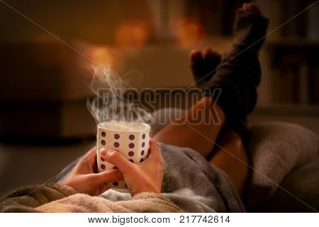 Woman with cup of hot drink  and feet lying on pilow in the cozy room