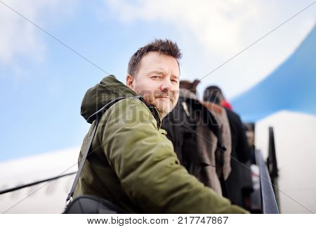 Middle age man during boarding on plane at aircraft in International airport. Passenger on ladder with airplane on background