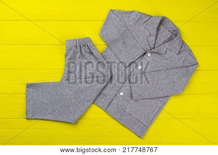 Boys pajama set on yellow table. Simple design and gray melange fabric. Comfy pants and shirt for good sleep.