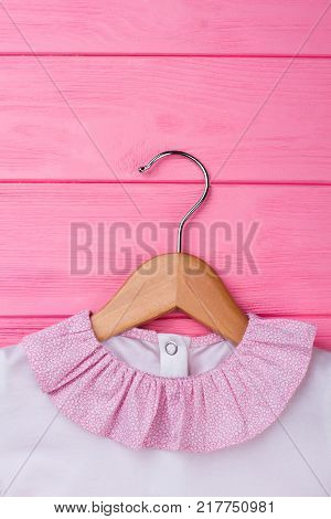 Kids garment on wooden hanger, close up. Cute ruffle collar on girls' blouse. Pink wooden background.