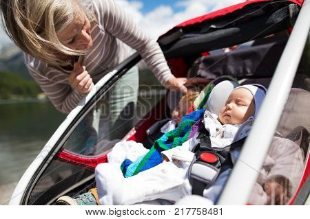 Senior woman and sleeping grandchildren in jogging stroller at he lake.