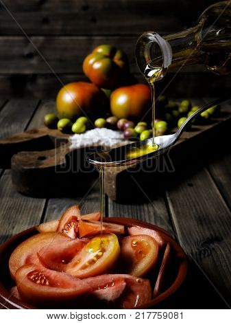 Close-up of an cruet pouring olive oil over tomato salad on an antique wooden table