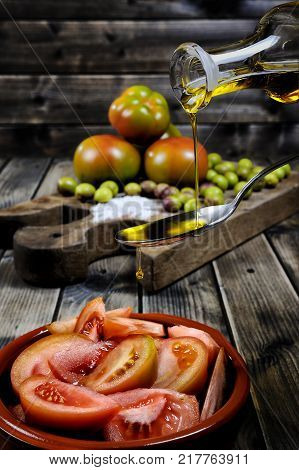 Close-up of an cruet pouring olive oil over tomato salad on an antique wooden table