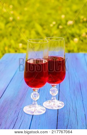 Two glasses with homemade red wine on blue boards outdoors in countryside at summer.