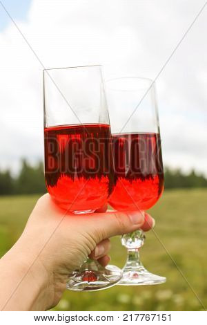 Two glasses with homemade red vine in a hand on farm yard background in countryside at summer.