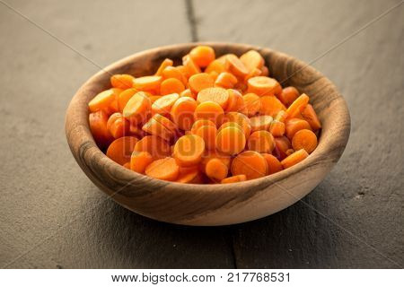 Carrot slices in wooden bowl. Fresh cut crisp slivers of Daucus carota, a root vegetable with orange color. Edible taproot pieces. Isolated macro food photo close up from above