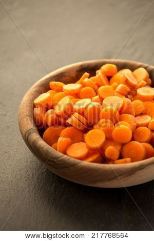 Carrot slices in wooden bowl. Fresh cut crisp slivers of Daucus carota, a root vegetable with orange color. Edible taproot pieces. Isolated macro food photo close up from above