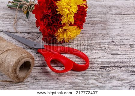 A bouquet of carnations tied with a rope in the upper left corner. With a skein of threads and scissors are shown not completely on a wooden background close-up