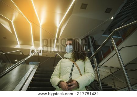 Person wearing protective mask against transmissible infectious diseases and as protection against pollution and the flu. Woman in a shopping center on an escalator