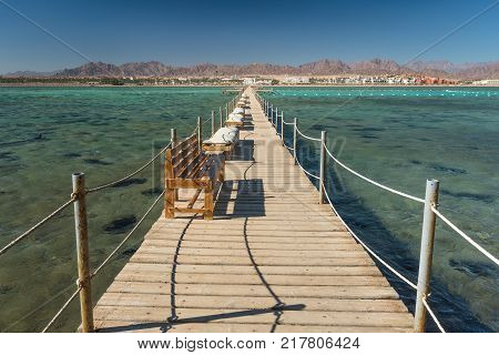 Pier with chaise longues in the sea in resort. Summer vacation. View at a clear sea with turquoise water. Summer vacation at a sea coastline in a exotic country.