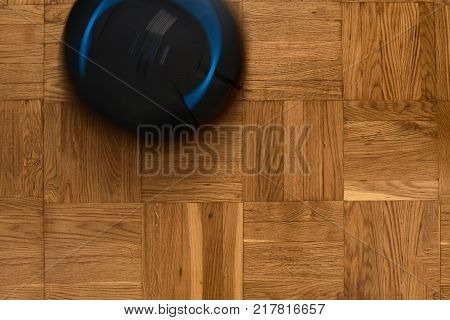 Top view of robotic vacuum cleaner on wooden parquet floor, natural movement, natural motion blur