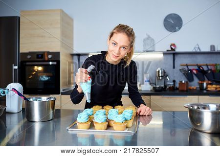 The confectioner with a pipping bag of cream in his hands decoretion cupcake on the table in the kitchen of a pastry shop.