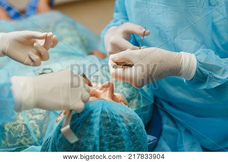 Male Old Professional Dentist Surgeon In Uniform And Female Assistant Helps To Performing Operation