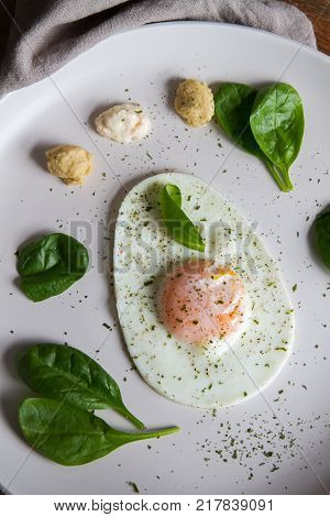 Single Fried Egg In Egg Shape Over White Plate Garnished With Spinach Green Herbs Salt Papper Horser