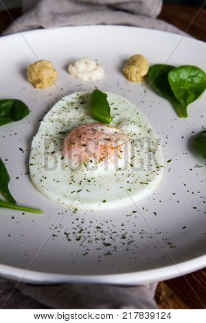 Single Fried Egg In Egg Shape Over White Plate Garnished With Spinach Green Herbs Salt Papper Horser