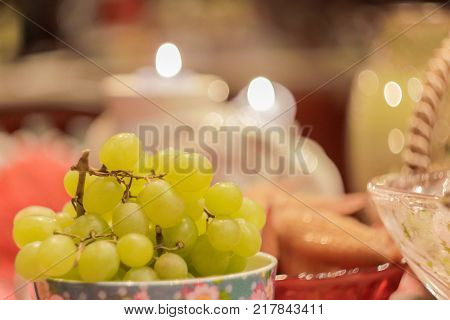 Green grapes on a table amidst smoldering candles