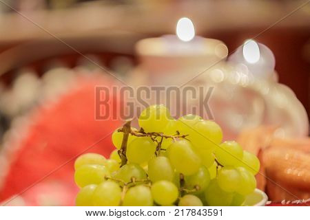 Green grapes on a table amidst smoldering candles