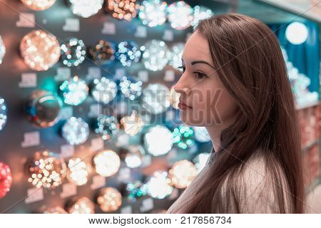 Dreaming customer girl choosing Christmas tree decorations - garlands. difficult decision. Various choice