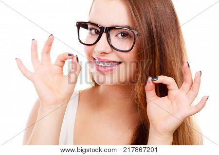 Vision and dentistry problems concept. Happy nerdy teenage wearing big eyeglasses showing her braces on teeth a ok gesture.