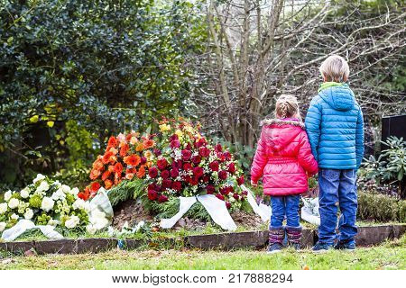 Little brother and sister standing at the grave of their parents in the graveyard