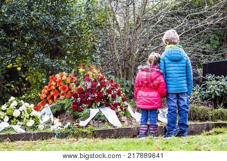 Little brother and sister standing at the grave of their parents in the graveyard