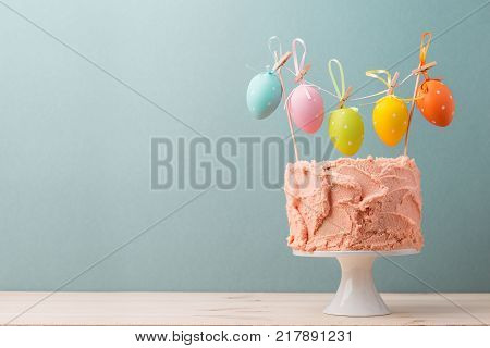 Arrangement of colorful Easter eggs on top of frosted cake served on blue background.
