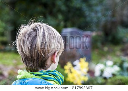 Little boy standing at the grave of his parents in the graveyard