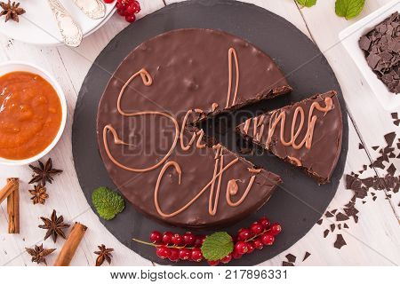 Sachertorte with red currants on black dish.