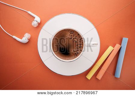 Orange background as a symbol of cheerfulness. A cup of fragrant coffee music and colored chalk is a creative and cheerful morning.