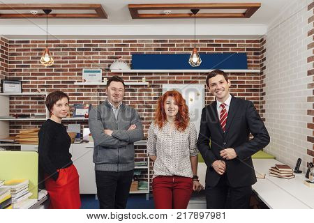 Portrait Of Office Staff Standing In Office. Team is looking at camera and smiling while standing in thei working space.