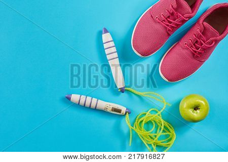 Flat lay of female sport equipments in pink color with jump rope and sneakers on blue background. Sports and healthy lifestyle concept. Top view. Copy space. Still life