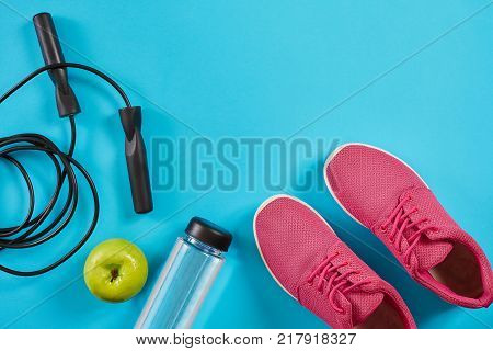 Flat lay of female sport equipments, jump rope, bottle of water and pink sneakers on blue background. Sports and healthy lifestyle concept. Top view. Copy space. Still life