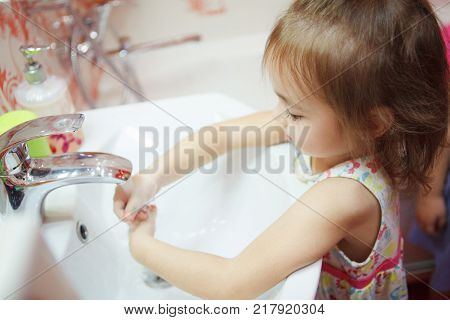 Kid with fair hair, wearing t-shirt and thoroughly washing hands in bathroom with water and soap, following rules and maintain hygiene, healthy lifestyle of child