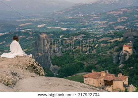 Alone female in the white plaid on the edge of the rock look on the monasteries of Meteora. Female on the rock and monasteries of Meteora in Greece in Thessaly at the early morning
