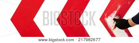 a man's hand in a black cloth glove holds a paintbrush and draws a red direction arrow on a white wall