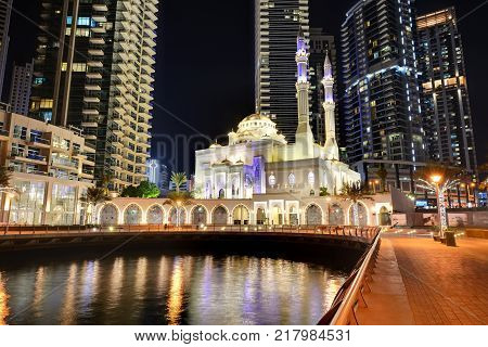 DUBAI UAE - NOVEMBER 19: The night illumination of Dubai Marina and Muslim Mosque on November 19 2017 in Dubai UAE. It is an artificial canal city built along a two mile (3 km) stretch of Persian Gulf shoreline.