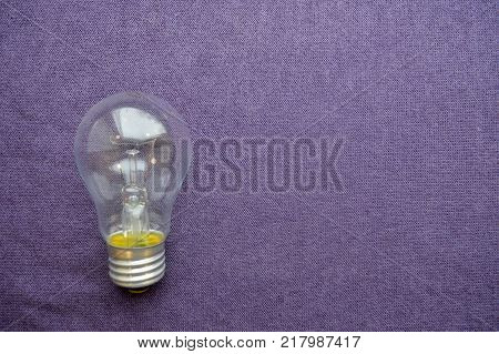 A round ordinary non-economical incandescent bulb with a transparent socle background of purple cloth.