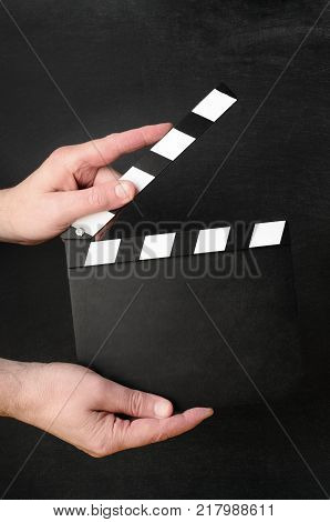 A blank clapperboard held open as if about to snap shut between the hands of a male operative with black chalkboard background.