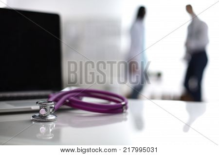 Laptop and medical stethoscope on the desk , doctors standing in the background.