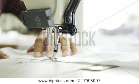Close up of an unrecognizable semstress hands sewing a white shirt at a factory. She is using a sewing machine. Locked down real time close up shot