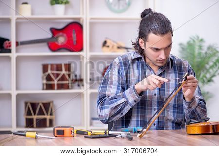 Young handsome repairman repairing violin
