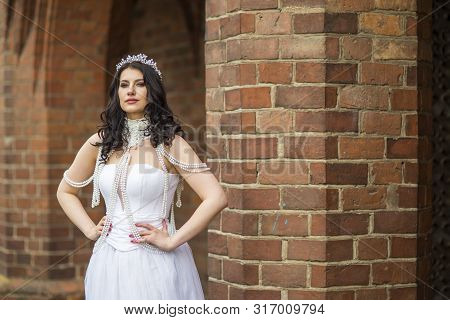 Portrait Of Tranquil Sensual Caucasian Bride With Crown And Necklace Posing Against Old Brick Wall O