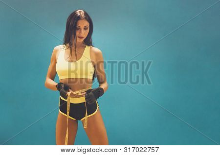 Beautiful Athletic Girl In Yellow Top And Black Shorts Standing At Blue Wall And Holding Measuring S