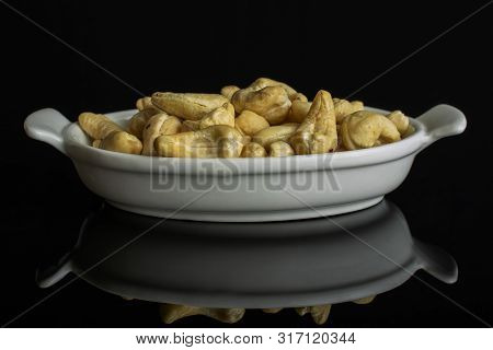 Lot Of Whole Unsalted Beige Cashew In White Oval Ceramic Bowl Isolated On Black Glass