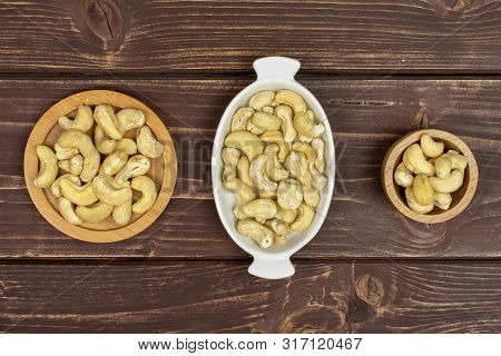 Lot Of Whole Unsalted Beige Cashew On Round Bamboo Coaster In Tiny Wooden Bowl In White Oval Ceramic
