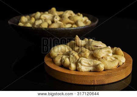 Lot Of Whole Unsalted Beige Cashew On Round Bamboo Coaster In Dark Ceramic Bowl Isolated On Black Gl