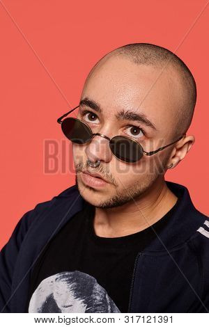 Studio Shot Of A Young Tattoed Bald Man Posing Against A Pink Background. 90s Style.