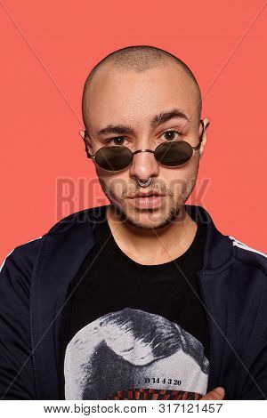 Studio Shot Of A Young Tattoed Bald Man Posing Against A Pink Background. 90s Style.