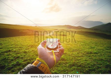 Male Hand With A Magnetic Compass Ea Against The Backdrop Of A Beautiful Landscape At Sunset. The Co
