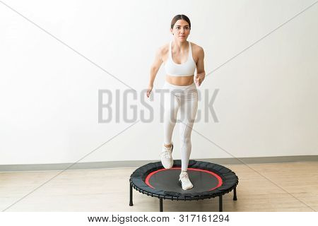 Dedicated Young Woman In White Sportswear Trampolining Against Wall During High Intensity Interval T